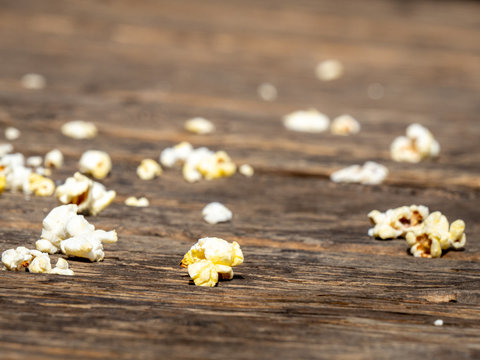 Close up of popcorn carelessly spilled on wooden boardwalk with selective focus and room for copy