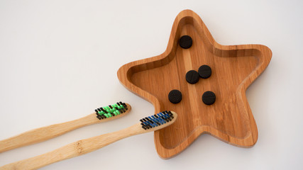Two bamboo toothbrushes, bamboo star shape plate with charcoal pills white background