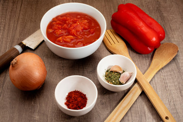 Ingredients for a tomato sauce with bell peppers, ground chili, onion, garlic, parsley and organic tomato puree on a rustic wooden table in a 45 degree view.