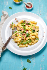 Italian recipe Pasta tortilloni with green pea, mint leaves, cheece, smoked bacon and cheese. Top view, blue background.