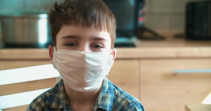 Small boy in quarantine at home look at camera in blue medical mask is struggling with illness epidemic control of coronavirus and proper infection prevention protection health virus flu face allergy