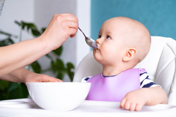 baby food. Mom feeds little caucasian child. healthy porridge, mother hands with spoon. Newborn infant kids.