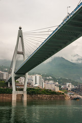 Xinling, China - May 6, 2010: Xiling gorge on Yangtze River. Under Part of Badong suspension bridge above green water and highrise buildiings Descending cloudscape over green mountain range.