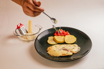 Grilled chicken breast with ham and cheese, accompanied by roasted apples, red pepper and garnished with a rosemary flower. Served on a green plate and a white background. with Parmesan cheese.