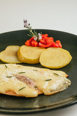 Detail of grilled chicken breast with ham and cheese, accompanied by roasted apples, red pepper and garnished with a rosemary flower. Served on a green plate and a white background.