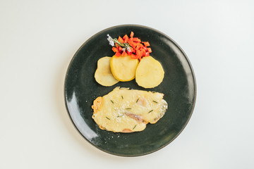 Aerial image. Grilled chicken breast with ham and cheese, accompanied by roasted apples, red pepper and garnished with a rosemary flower. Served on a green plate and a white background.