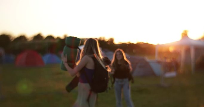Vintage long haired caucasian girls at festival camping site in sunset throwing camping gear op in the air in slow motion