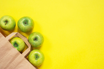 Some green apples rolling out from the cardboard package on bright yellow surface. Craft organic pack and natural product, ecological healthy concept.