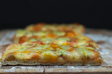 Flat bread pizza by cheese on a cutting board with flour in black background