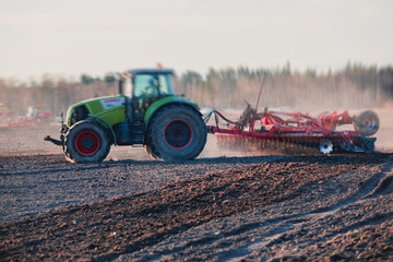 Tractor with a disc harrow system harrows the cultivated farm field, process of harrowing and...