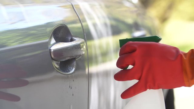 Nettoyage par d&eacute;sinfection du coronavirus en pulv&eacute;risant un antisepsie assainissent sur une poign&eacute;e de porte de voiture, muni de gant de protection.