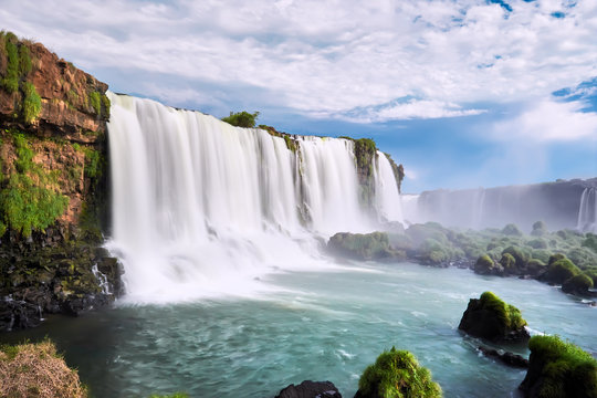 Iguazu waterfalls in Argentina, view from Devil's Mouth. Panoramic view of many majestic powerful water cascades with mist. Panoramic image with blue sky and clouds.