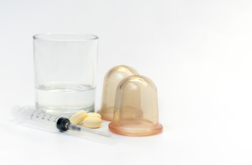 Medical syringe, pills, massage jars and a glass of water close-up on a white background, shallow depth of field.