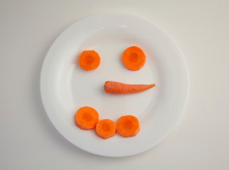 cheerful smiley from peeled fresh carrots sliced in circles and small carrots on a white plate white isolated background