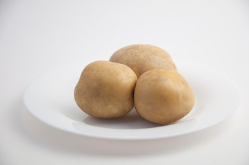 three fresh potatoes on a white plate and white closeup isolated background