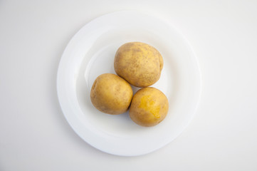 three fresh potatoes on a white plate and white closeup isolated background