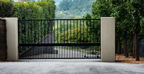 Black metal wrought iron driveway property entrance gates set in brick fence, concrete path, garden...