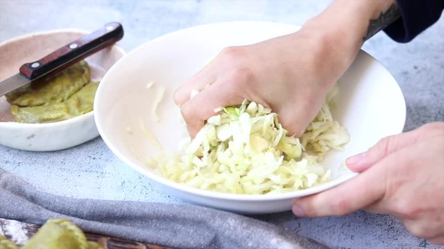 Woman crush and wrinkle white chopped cut cabbage salad in bowl on table for sauerkraut. Make vegan food.