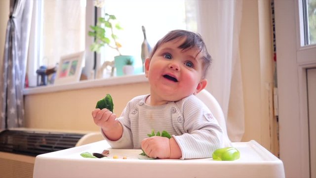Little toddler infant boy eat first supplementary vegetarian food. Vegan baby try cucumber and smile in highchair.