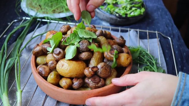 Woman hands add rucola herb to baked,  grilled potato with mushrooms . Vegan food lunch. 