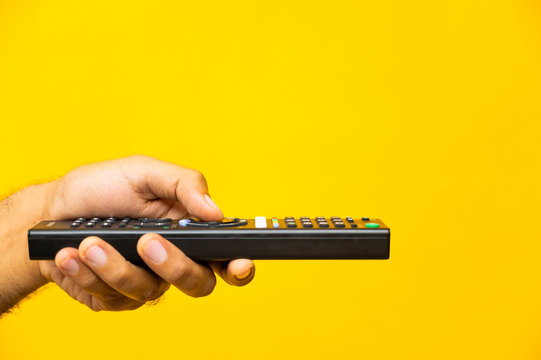 Close up male hand holding television remote control on isolated yellow background.