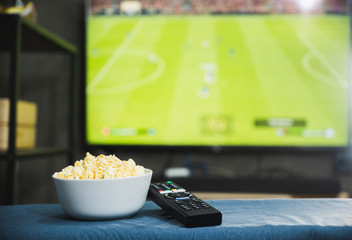 Popcorn and television remote control on football program tv screen background. Watching tv relax...