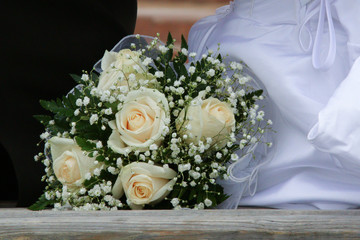 white roses bride's bouquet on a bench.  Bride and groom are in the background