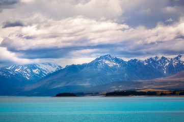Obraz premium Dramatic view of Lake Pukaki with the snow-capped mountain peaks lost in clouds. The alpine lake is famous for the amazing turquoise hues of the water in New Zealand, South Island.