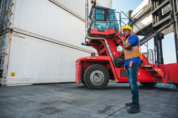 Black foreman worker working control the crane and forklift at Container cargo harbor to loading containers. African dock male staff for Logistics import export shipping concept.