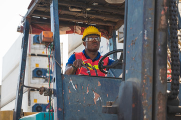 Black foreman worker driving forklift checking at Container cargo harbor to loading containers and...