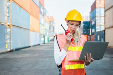 Foreman woman worker working checking at Container cargo harbor holding laptop computer and radio walkie-talkie to loading containers. Dock female Logistics import export shipping concept.