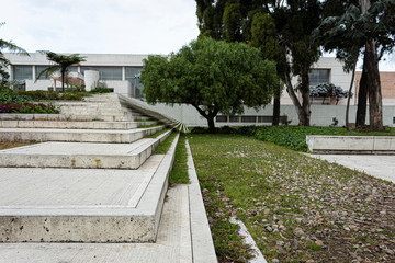 Geometric pattern of a modern white street stairways with green gardens, trees and big building at background