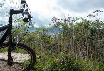 Fototapeta na wymiar City landscape at the top of mountain view with green vegetation and black mountain bike front, handle bar and front tire
