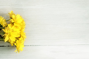 a sprig of yellow chrysanthemum flowers on a white wooden background