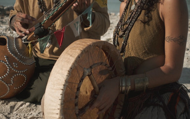 Close up woman hoolding drum and man playing on sitar sitting on sand