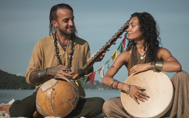 Ethnic woman and man musicians with accesories and musical instruments on the beach with sea on...