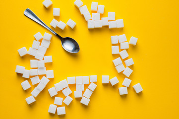 Refined sugar cubes and teaspoons shot on a yellow background. Background for sweets, and cutlery.