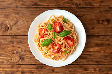 Pasta in tomato sauce with cheese and basil on a wooden background