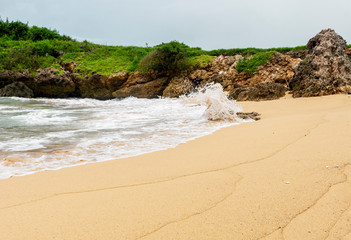 A clean beach with an ocean wave surrounded by rocks