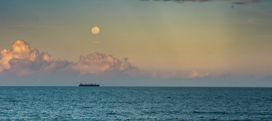 A ship on the ocean with clouds and moon rising behind it