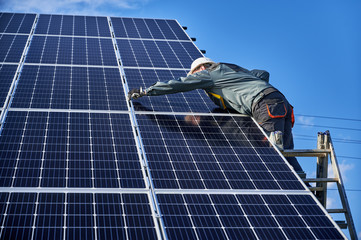 Professional electrician standing on ladder and installing photovoltaic solar panel system. Man...