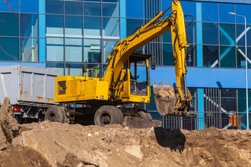 Excavator loader and dump truck during earthworks at a construction site. Loading land in the back of a heavy truck. Excavator digs land for the construction of a new park area.