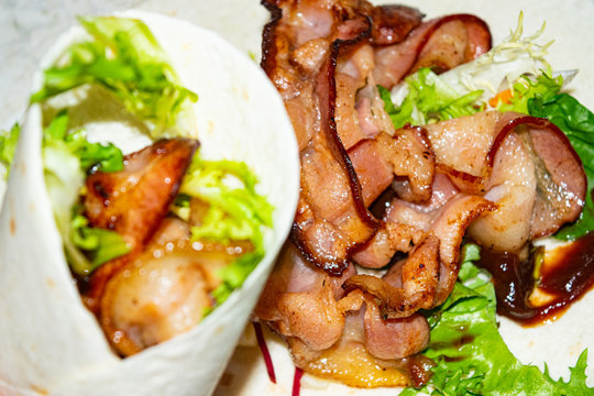 Leafy salad, sliced vegetables, sauce and fried bacon slices wrapped in pita bread. Delicious homemade Shawarma. Close up.