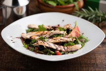 Roasted chicken with rocket salad in white bowl on wood table