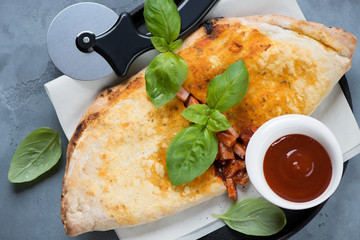 Top view of pizza calzone with prosciutto and mozzarella cheese, horizontal shot on a grey concrete background