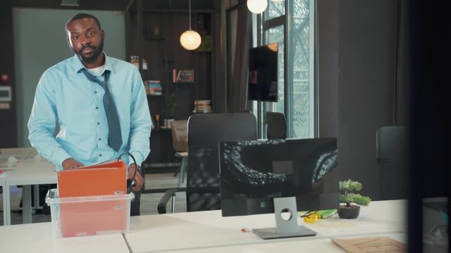 Sad African american man office worker packing a box with office stuff from his table and leaving an office fired ue to coronavirus crisis unemployed depression business low motion