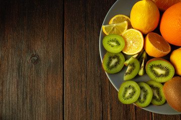kiwi, oranges and lemons on a plate on a dark wooden table