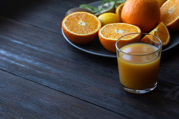 a glass of juice stands next to a plate of fruit on a dark wooden table in the kitchen
