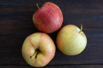 three apples with drops of water on a dark wooden background top view
