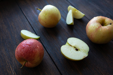 three apples with a slices of water drops on a dark wooden background